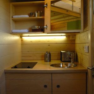 Hébergement insolite en bois avec kitchenette moderne et éclairage chaleureux.