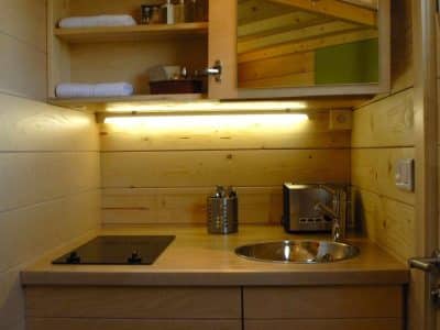 Hébergement insolite en bois avec kitchenette moderne et éclairage chaleureux.