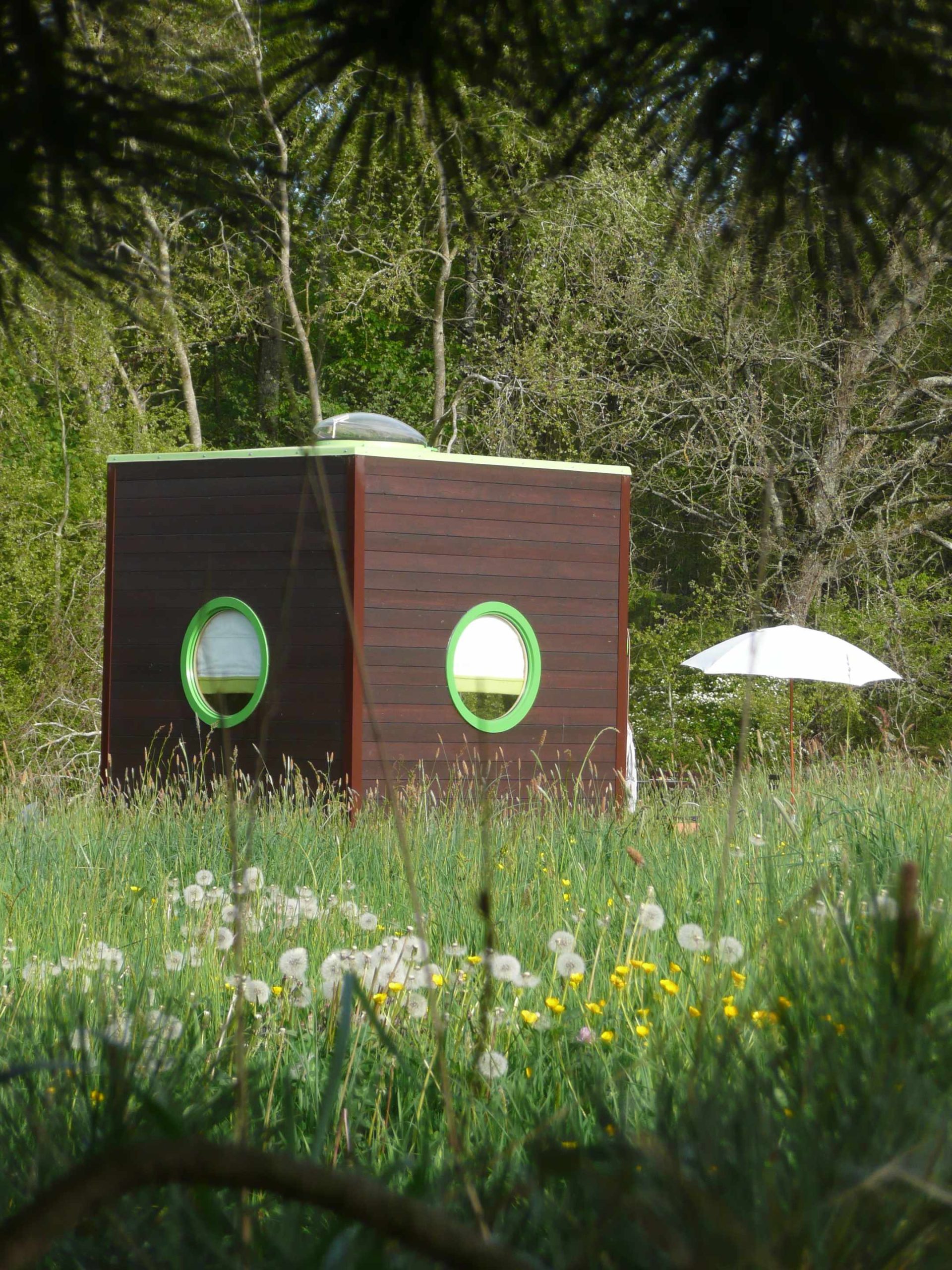 carre d'etoiles 3 Hébergement insolite en forme de cube, avec fenêtres rondes, entouré de fleurs.