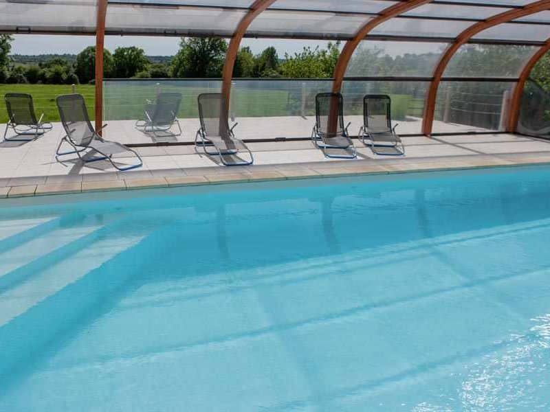 Gîte avec piscine couverte, chaises longues sur la terrasse ensoleillée.