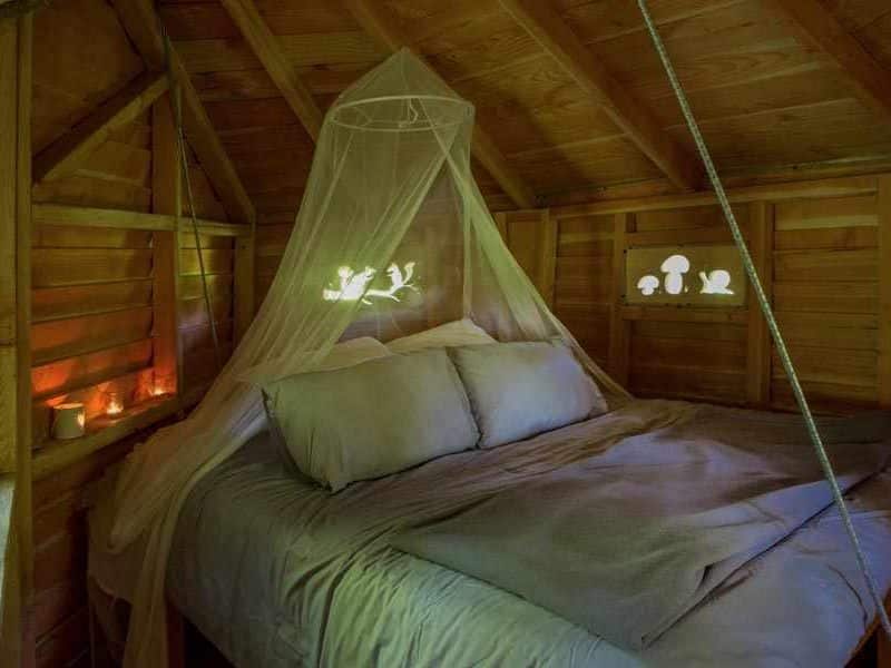Cabane en bois avec lit douillet, drap en voile et lumières douces.