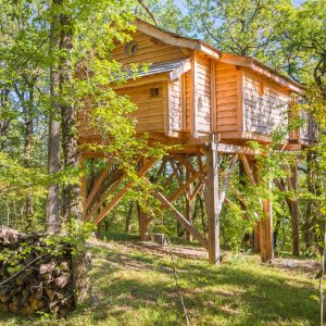 Cabane perchée en bois, entourée darbres verdoyants en Aquitaine.