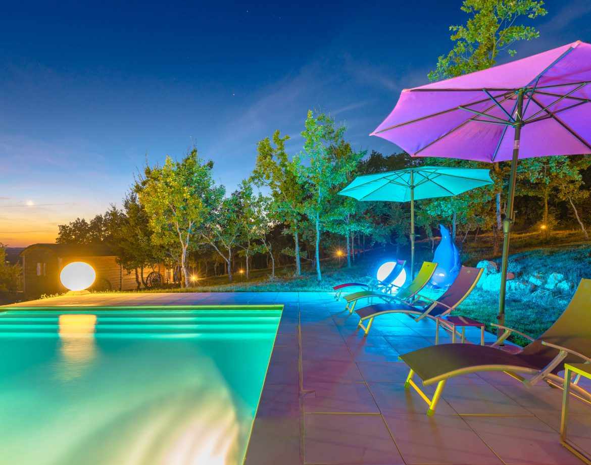 Hébergement insolite en Aquitaine avec piscine illuminée et parasols colorés.
