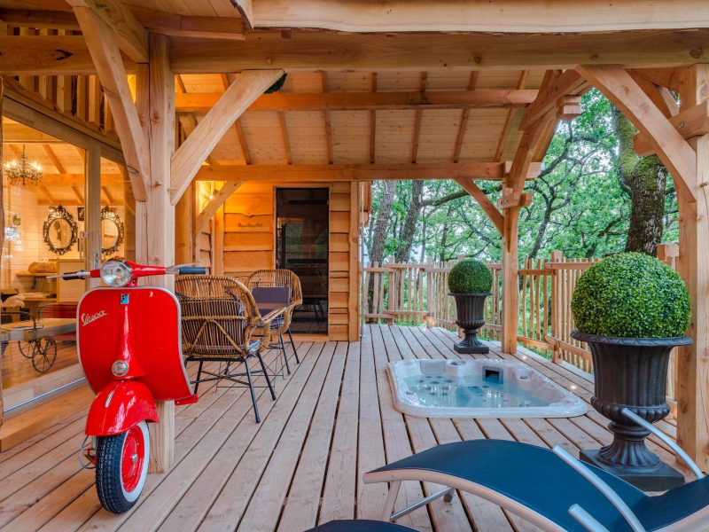Cabane en bois avec terrasse, scooter vintage et verdure environnante en Aquitaine.
