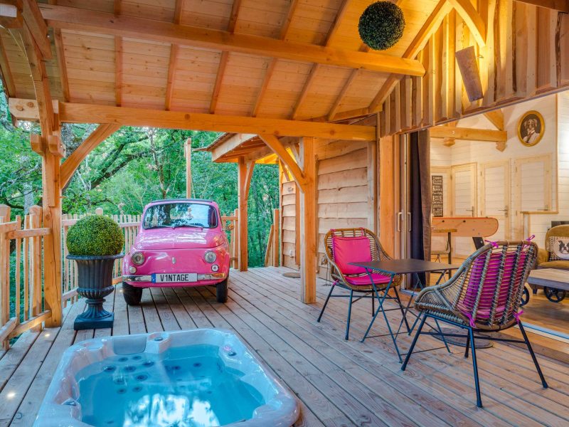 Cabane en bois avec jacuzzi, décor vintage et voiture rose sur la terrasse.