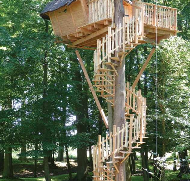 Cabane dans les arbres avec une terrasse en bois et un escalier spiral.