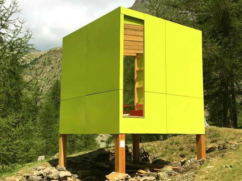 Cabane moderne et colorée, nichée dans la nature verdoyante des Alpes.