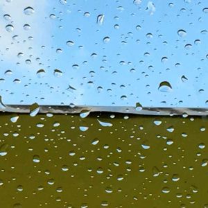 Vue à travers une fenêtre dun hébergement insolite en Provence, gouttes de pluie scintillantes.