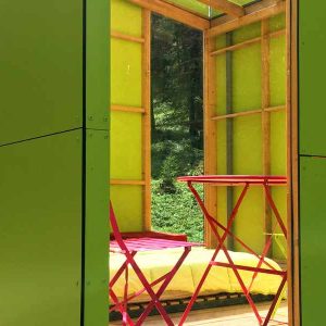 Cabane moderne en bois vert, avec un lit et une table rouge à lintérieur.
