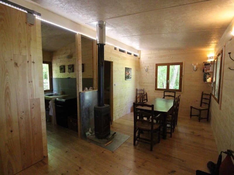 Chalet en bois spacieux avec poêle à bois et table pour repas conviviaux.