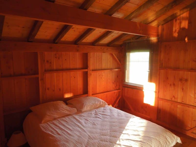 Chalet en bois chaleureux avec lit double et lumière naturelle.