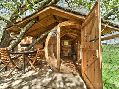 Cabane en bois perchée dans un arbre, avec une terrasse en bois et vue sur la nature.