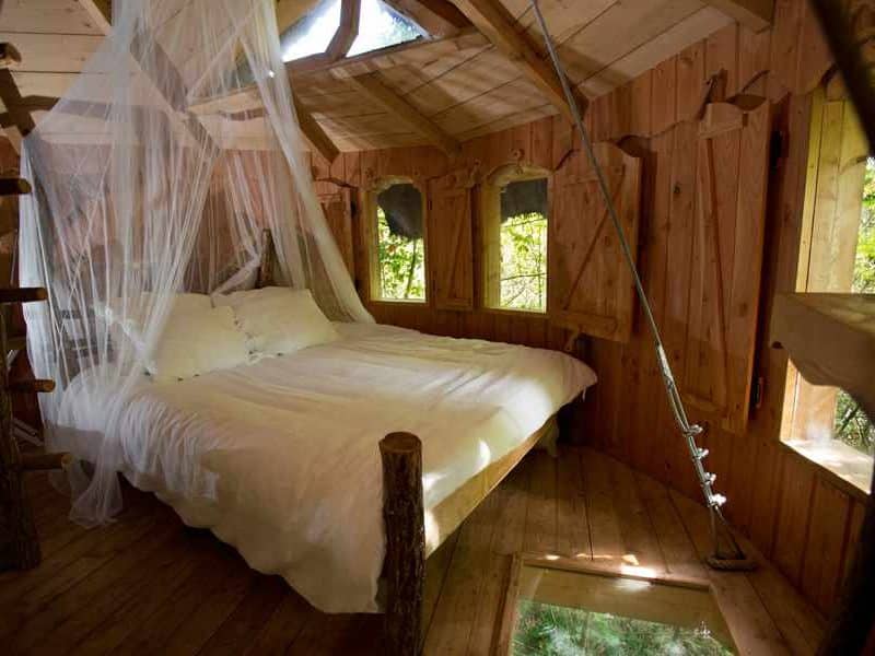 Cabane dans les arbres avec lit suspendu et moustiquaire, ambiance chaleureuse.