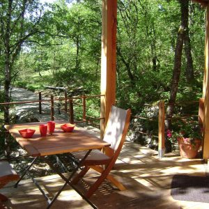 Cabane perchée en bois avec terrasse, entourée de verdure et vue sur la nature.