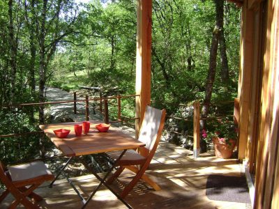 Cabane perchée en bois avec terrasse, entourée de verdure et vue sur la nature.