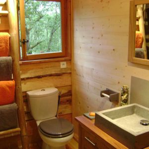 Salle de bain dun hébergement insolite en bois, avec lavabo en pierre et serviettes colorées.