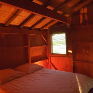 Chalet en bois chaleureux avec lit double et lumière douce filtrant par la fenêtre.