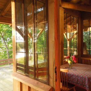 Cabane en bois avec grandes fenêtres, vue sur la nature et une table décorée de fleurs.