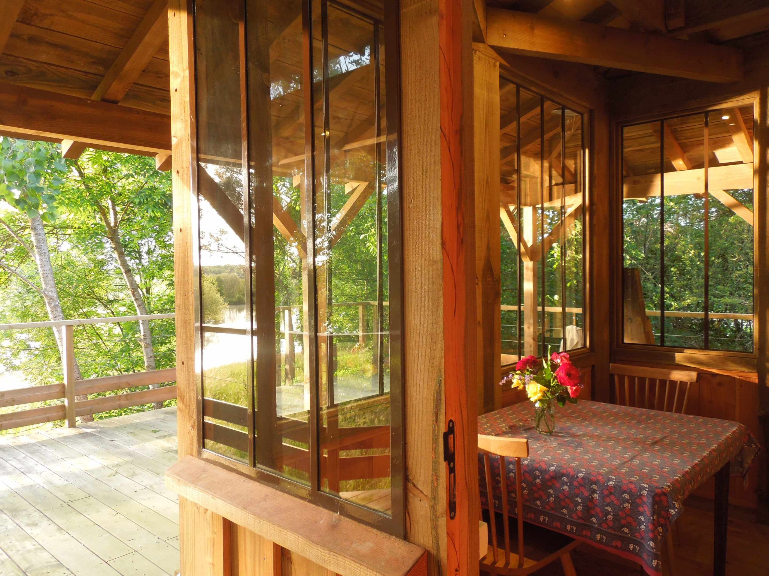 pb_09 Cabane en bois avec grandes fenêtres, vue sur la nature et une table décorée de fleurs.