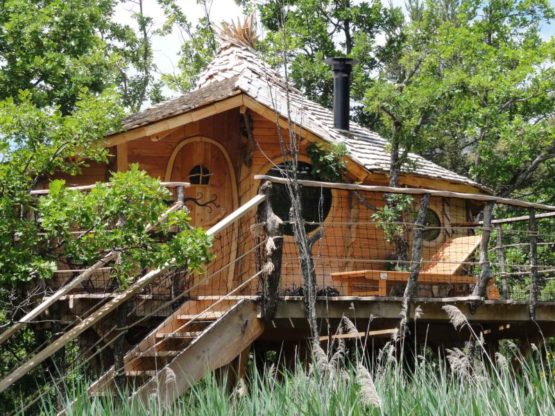 Cabane en bois perchée dans les arbres, avec un toit en bardeaux et un balcon.