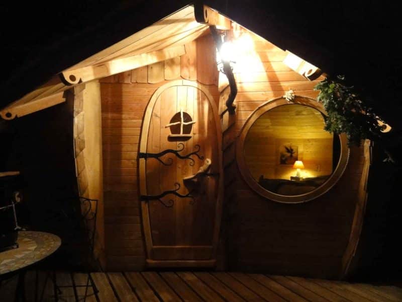 Charmante cabane en bois avec une porte sculptée et une lumière chaleureuse.