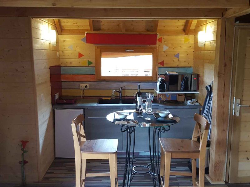 Chalet en bois avec cuisine équipée et coin repas lumineux.