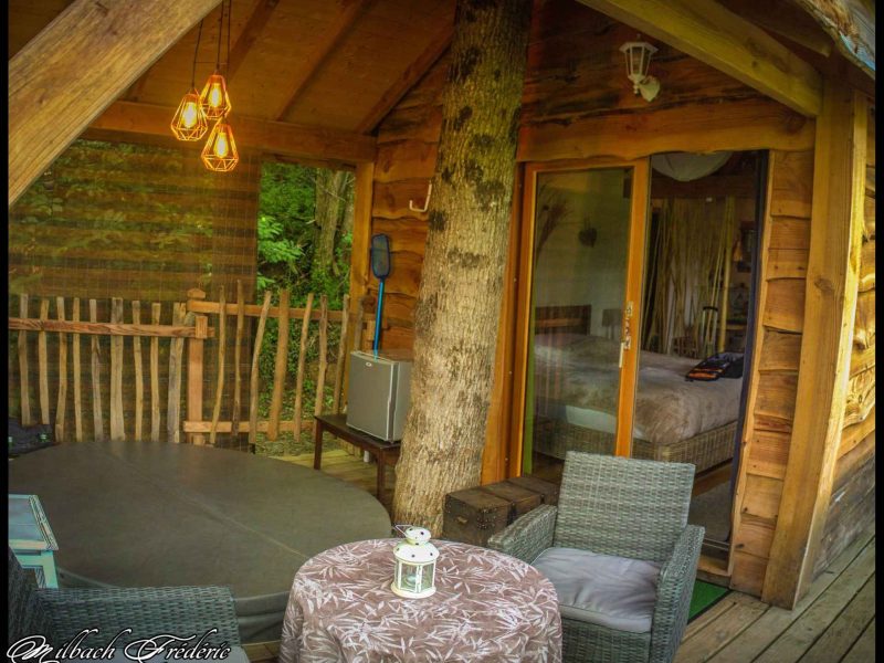 Cabane en bois avec terrasse, décorée de lanternes et vue sur la nature.