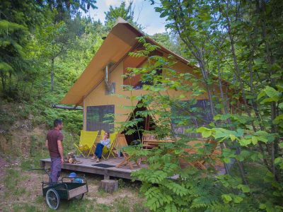 Cabane en bois dans la nature, avec terrasse et chaises jaunes, idéale pour se détendre.