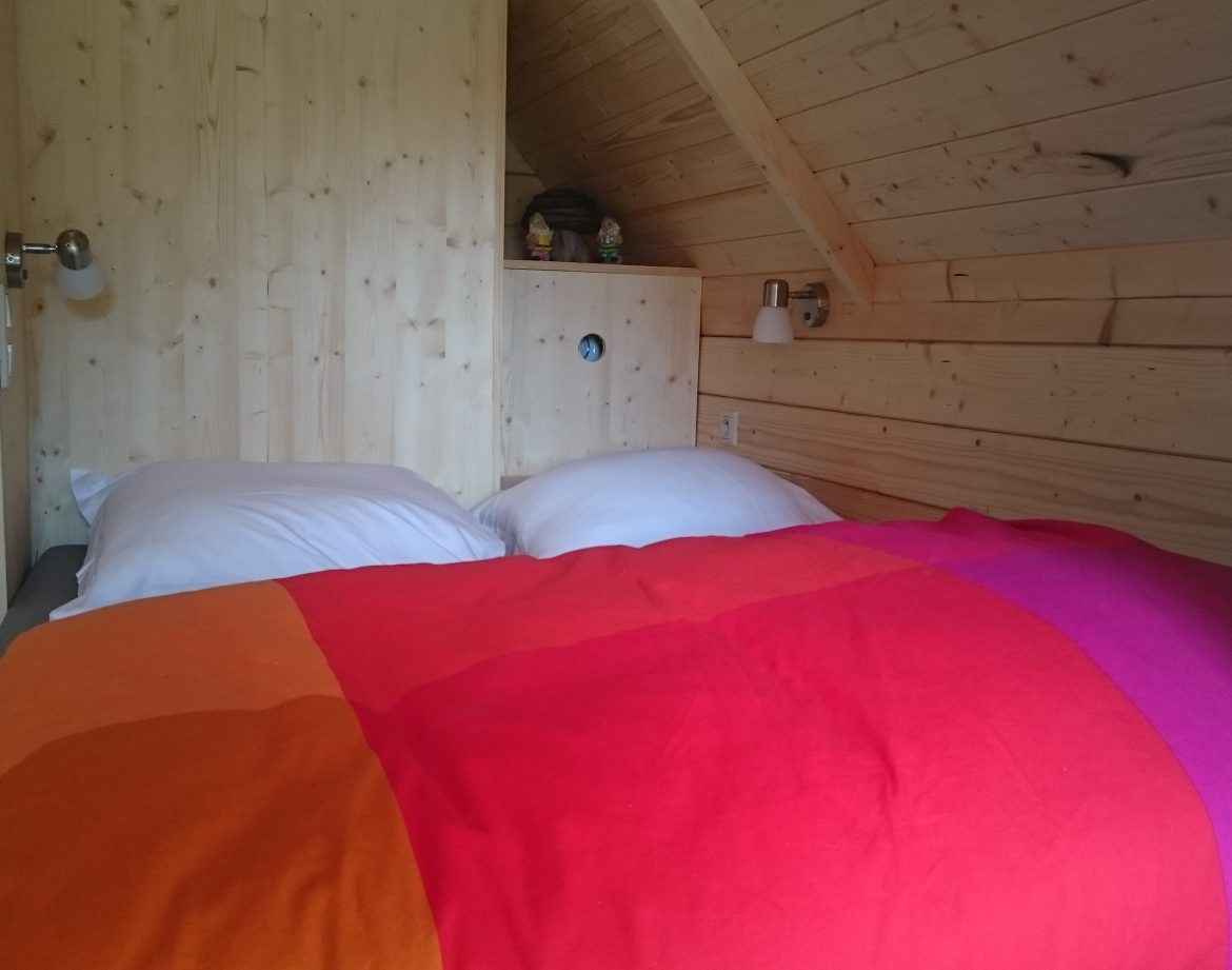 Chalet en bois chaleureux avec un lit coloré et des murs en bois naturel.