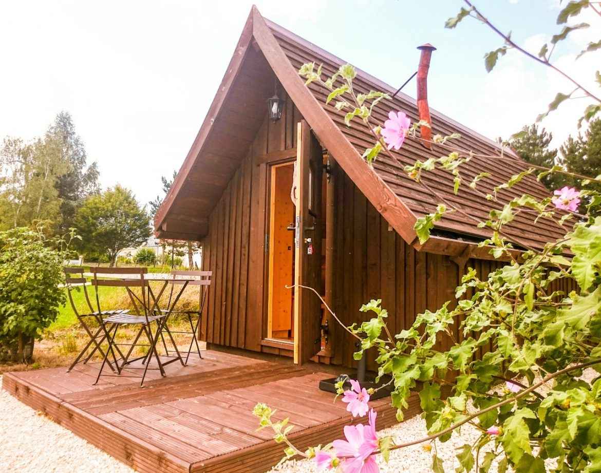 Cabane en bois avec terrasse, entourée de fleurs, au cœur de la nature.
