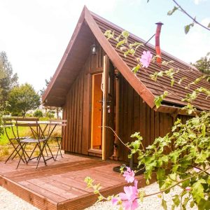 Cabane en bois avec terrasse, entourée de fleurs, au cœur de la nature.