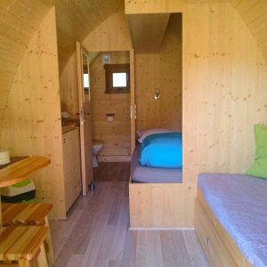 Hébergement insolite en bois, intérieur chaleureux avec lit et coin repas.