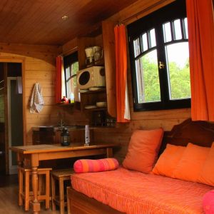 Hébergement insolite en bois avec un coin salon confortable et des rideaux orange.