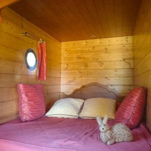Cabane en bois cosy avec lit douillet et coussins rouges, ambiance chaleureuse.