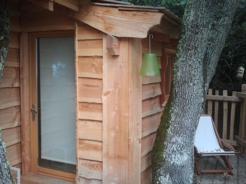 Cabane en bois nichée entre les arbres, avec une lampe verte suspendue.
