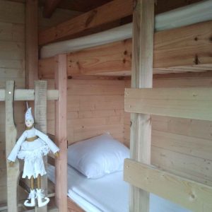 Cabane en bois avec lits superposés et une poupée en bois décorative.