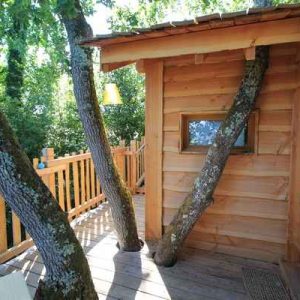 Cabane dans les arbres en Aquitaine, avec des troncs intégrés à la terrasse en bois.