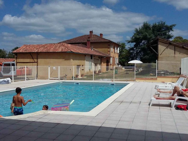 Gîte avec piscine extérieure, enfants jouant et transats au bord de leau.