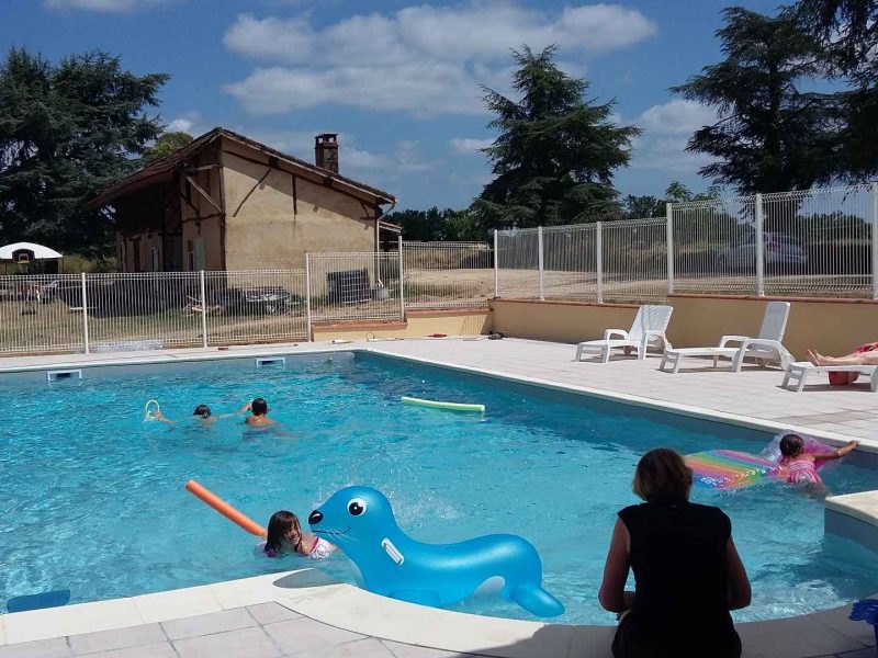 Gîte avec piscine extérieure, enfants jouant et chaises longues au soleil.