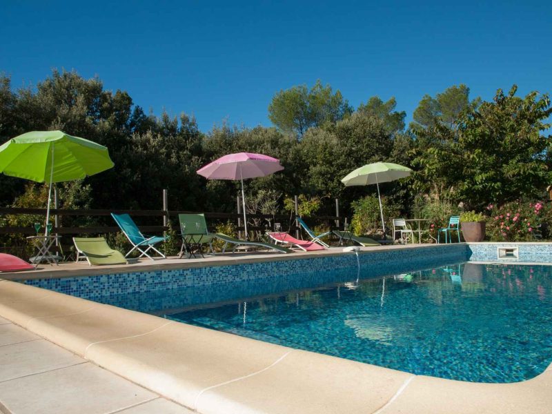 Hébergement touristique avec piscine, chaises longues et parasols colorés au bord.