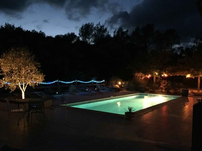 Villa avec piscine illuminée, entourée darbres et de lumières décoratives.