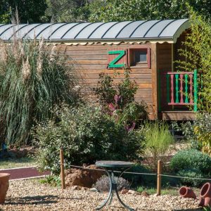 Charmante roulotte en bois, entourée de verdure et de plantes méditerranéennes.