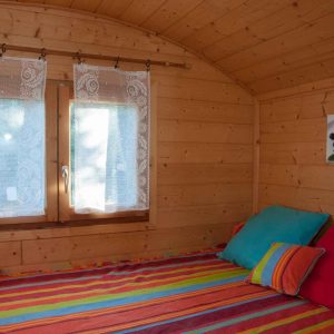 Chalet en bois coloré avec lit douillet et rideaux en dentelle, ambiance chaleureuse.