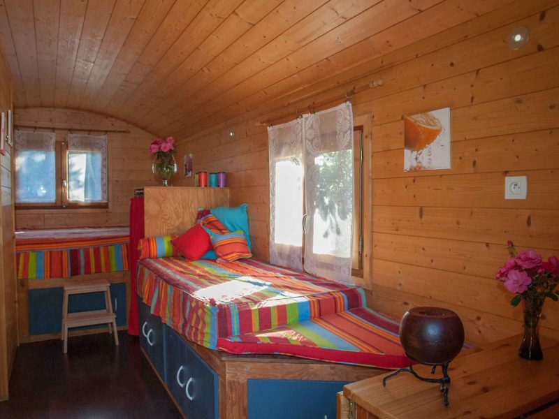 Chalet en bois chaleureux avec lits colorés et fenêtres lumineuses.