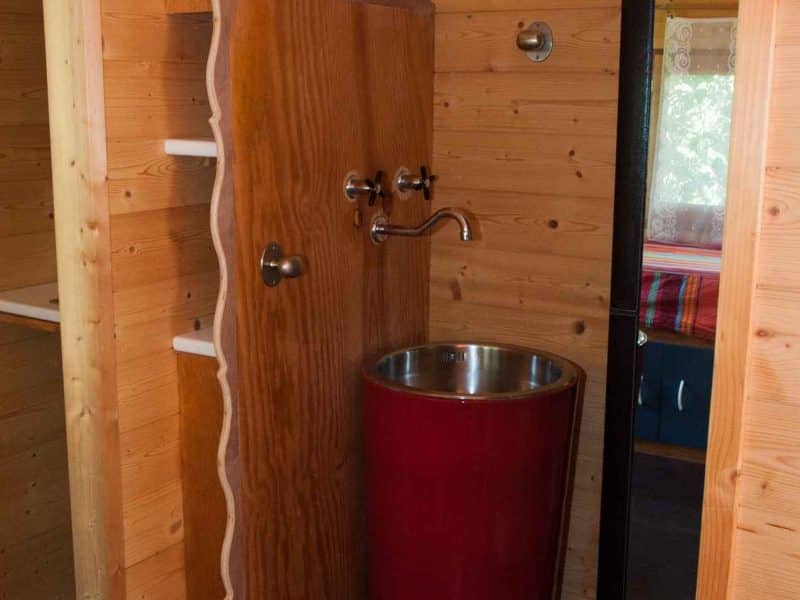 Cabane en bois avec lavabo rouge et miroir, ambiance chaleureuse et moderne.