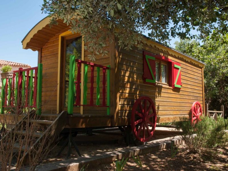Roulotte colorée en bois, entourée de verdure, idéale pour un séjour insolite en Provence.