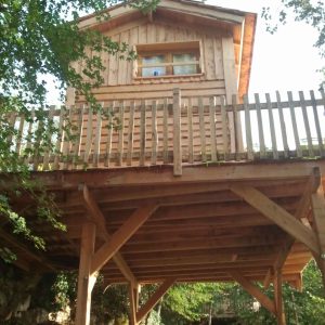 Cabane en bois sur pilotis, entourée darbres, offrant une vue paisible.
