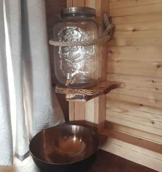 Cabane en bois avec distributeur deau en verre et bol en métal.