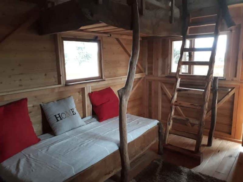 Cabane en bois avec un lit simple et des coussins rouges, ambiance chaleureuse.