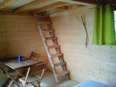 Cabane en bois avec échelle, décorée de bois naturel et rideaux verts.